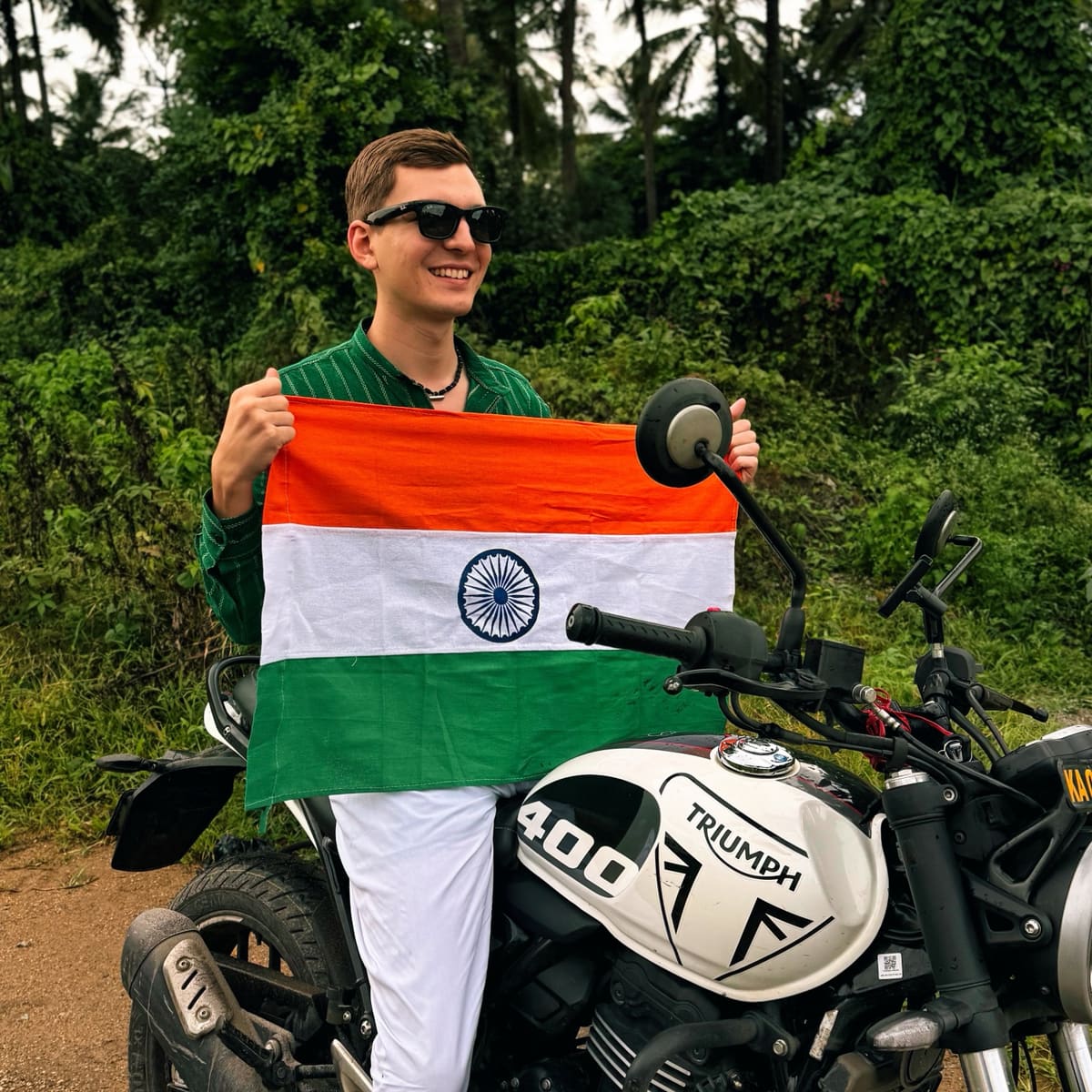 Alex Pervov holding the Indian flag beside a Triumph 400 motorcycle