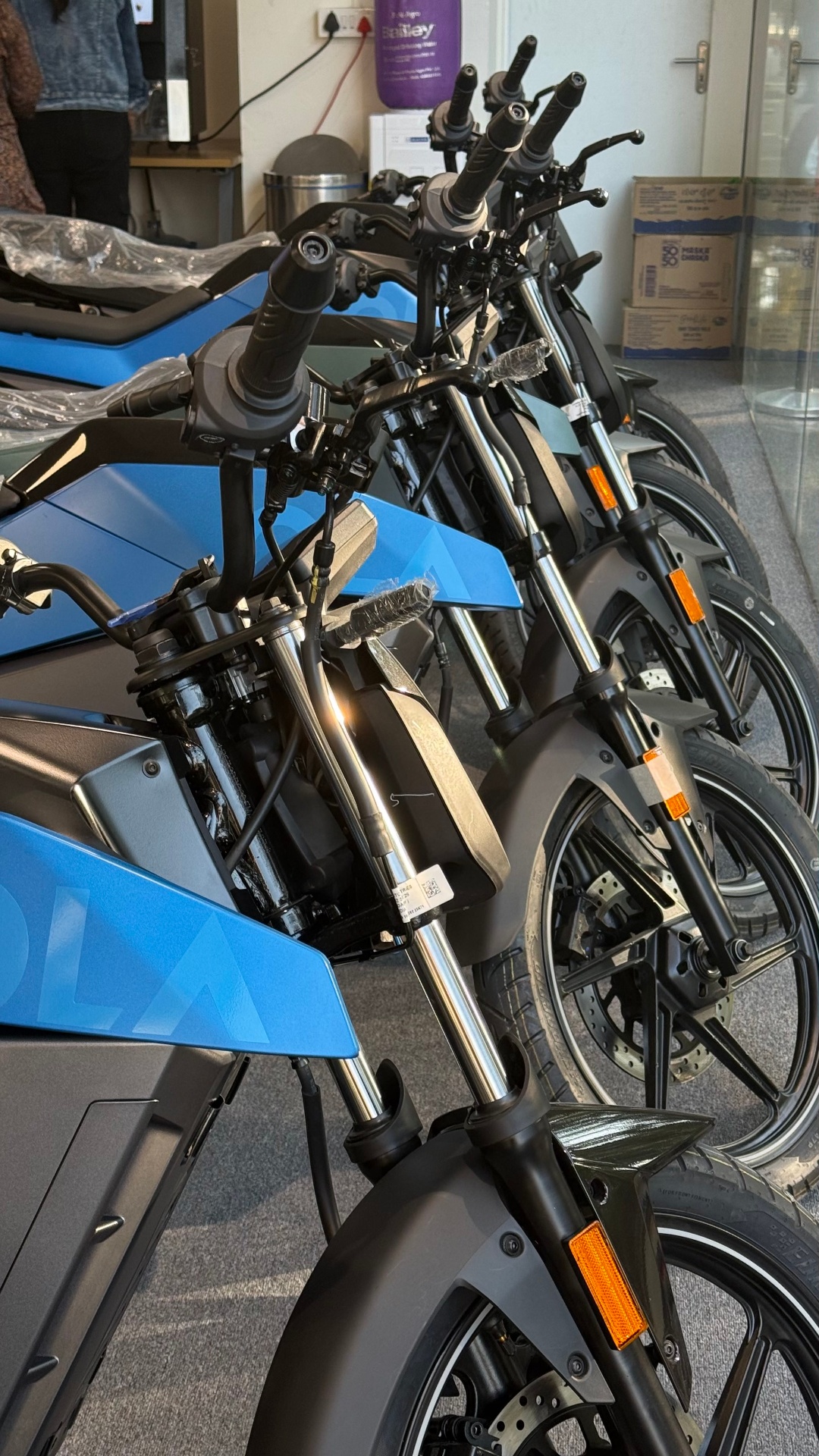Row of blue Ola Roadster electric motorcycles on display