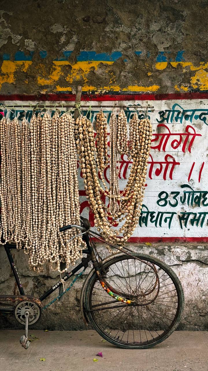 Prayer beads (mala) hanging on a bicycle against a colorful wall with Hindi text